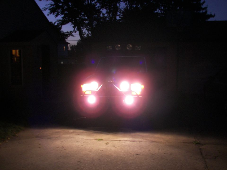 Front view of a vehicle at night with headlights and roof-mounted lights on