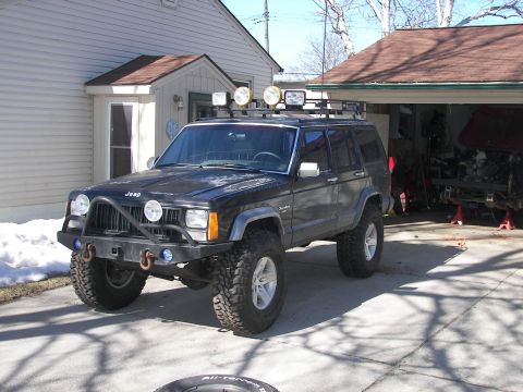 1988 Ford Bronco - A modified Jeep Cherokee XJ is parked in front of a house and garage.