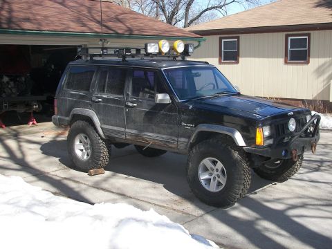 1988 Ford Bronco - This black Jeep Cherokee XJ features a roof rack with auxiliary lights and aggressive off-road tires.