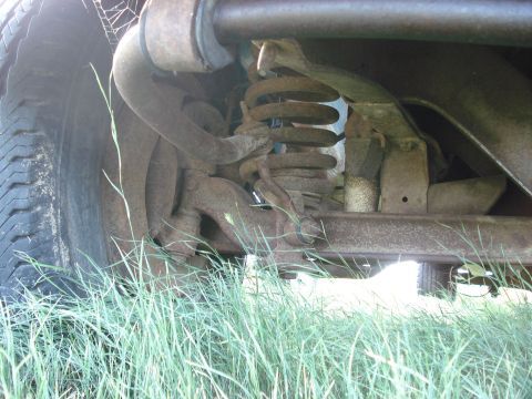 1979 Ford F-150 - Undercarriage view showing suspension components and a tire, partially obscured by grass.