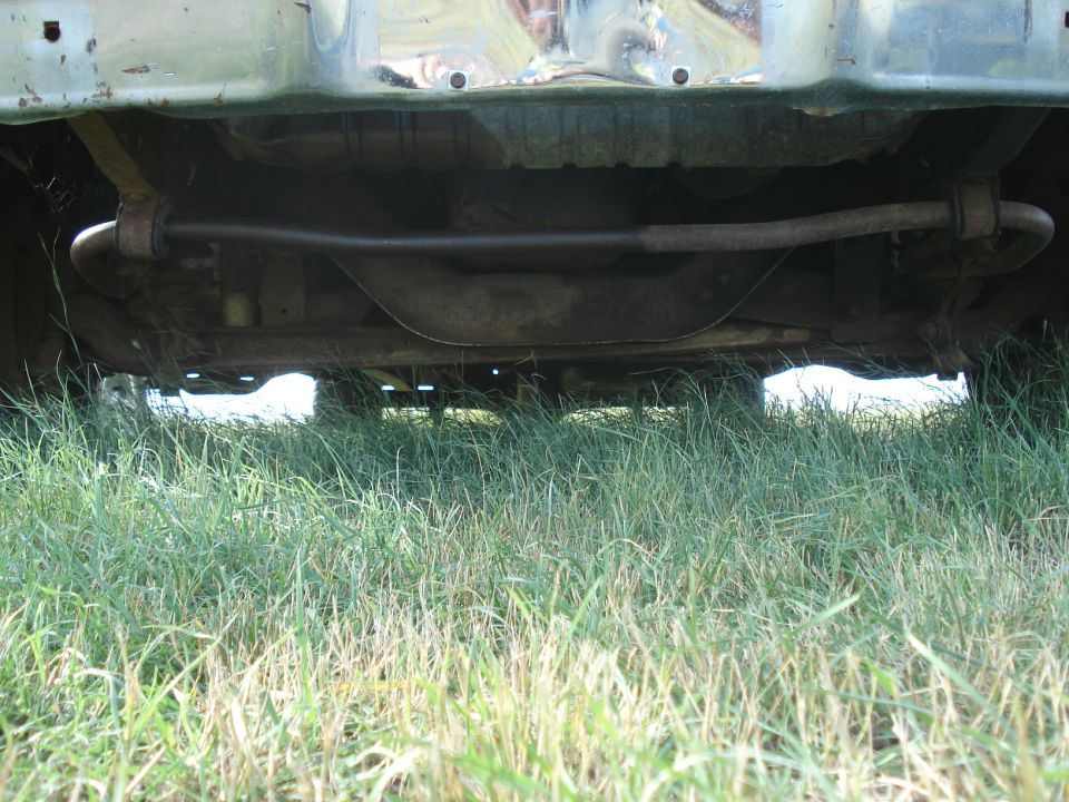 Underside view of a truck showing the front sway bar and suspension components. Grass is visible in the foreground and background