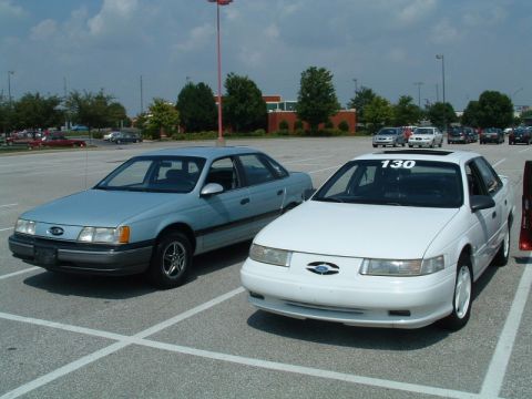 1993 Ford Taurus - Two Ford Taurus sedans are parked side-by-side in a parking lot under a cloudy sky.