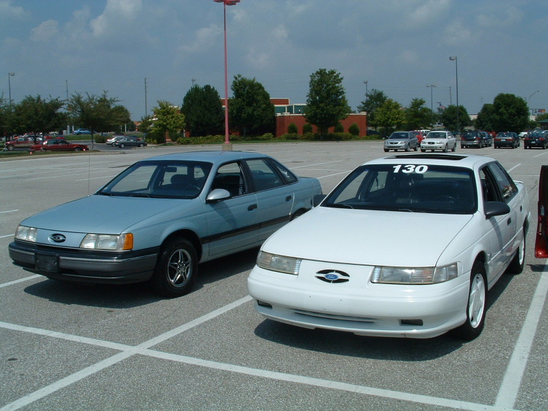 Light blue and white Ford Taurus sedans parked in a lot, one with a '130' sticker on the windshield