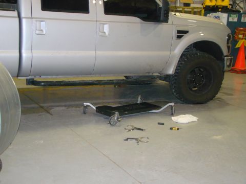 2008 Ford F-250 - A silver 2008 Ford F-250 pickup truck is shown from the side, with various tools and a creeper on the floor beneath it.