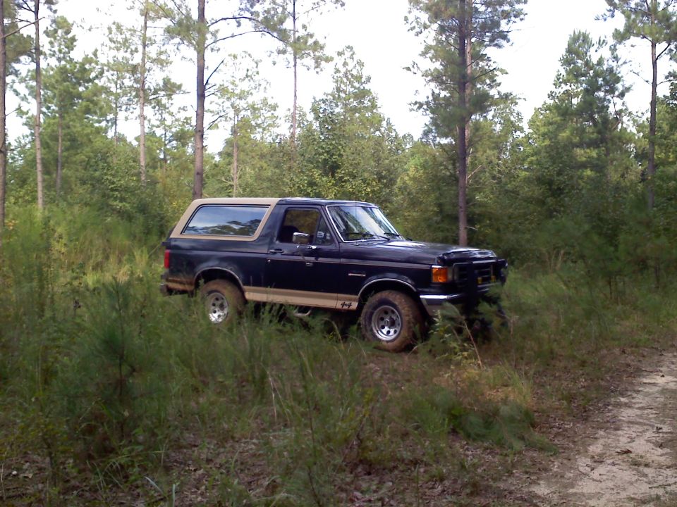 Dark blue 1990 Ford Bronco with tan top parked in grassy woods