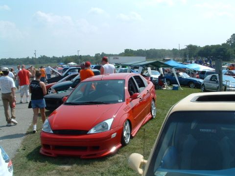 1993 Ford Taurus - Outdoor car show with multiple vehicles and attendees gathered on a sunny day.