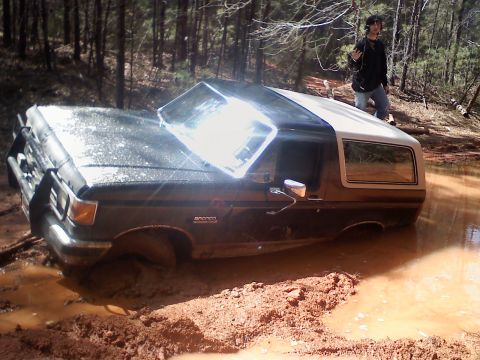1990 Ford Bronco - A person watches as a Ford Bronco is submerged in thick mud after an off-road excursion.