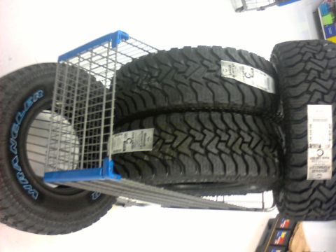 1990 Ford Bronco - Several off-road tires are stacked on a retail shelf, some with price tags attached.