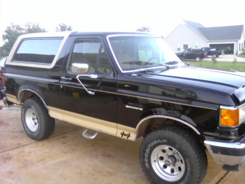 1990 Ford Bronco - This black Ford Bronco features tan trim and 4x4 badging, parked in a driveway.