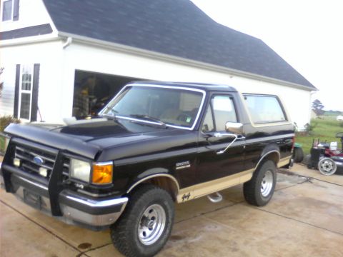 1990 Ford Bronco - Black 1990 Ford Bronco with tan trim and a bull bar is parked in front of a house.