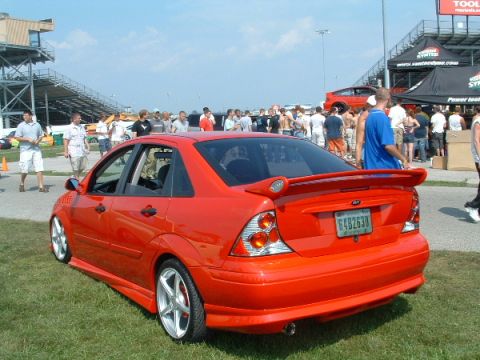 1993 Ford Taurus - A red sedan with a custom body kit and spoiler is parked on the grass at an outdoor event.