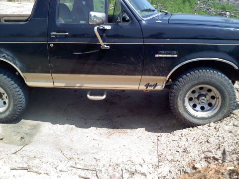 1990 Ford Bronco - The side of a black 1990 Ford Bronco is shown with tan trim and 4x4 decals.