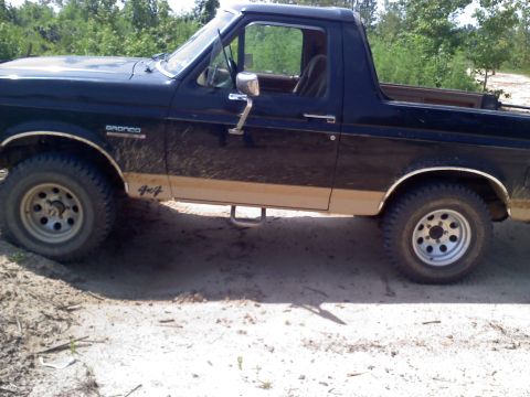 1990 Ford Bronco - This 1990 Ford Bronco 4x4 is seen in profile on a dirt path, with its distinctive two-tone paint scheme visible.