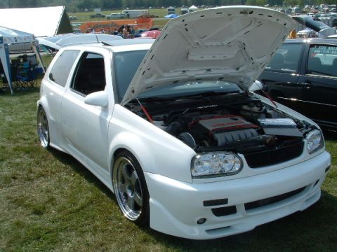 1993 Ford Taurus - A white hatchback is displayed with its hood open, revealing the engine bay and custom modifications.