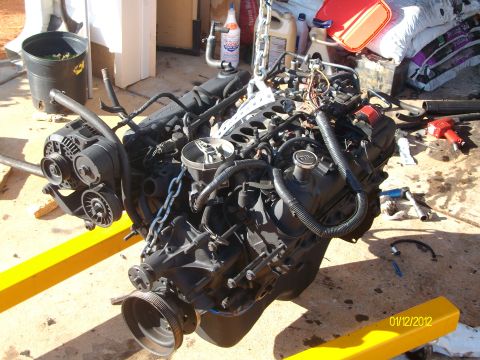 1990 Ford Bronco - Engine assembly, likely removed from a vehicle, is suspended by a hoist with surrounding tools and supplies.