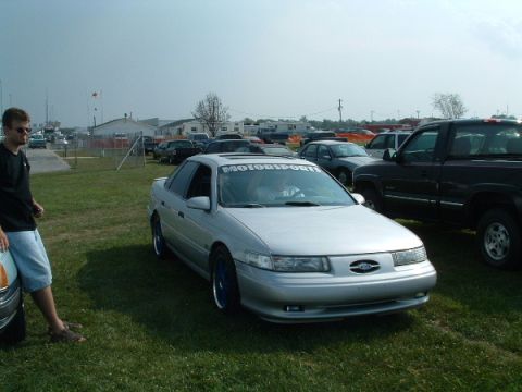 1993 Ford Taurus - A silver 1993 Ford Taurus is parked on grass at an outdoor event, with a 'motorsports' banner visible on its windshield.