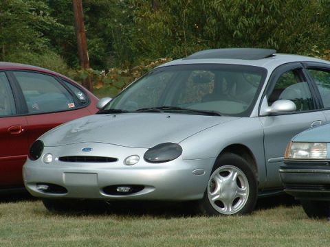 1993 Ford Taurus - A silver sedan is parked on a grassy area with trees in the background.