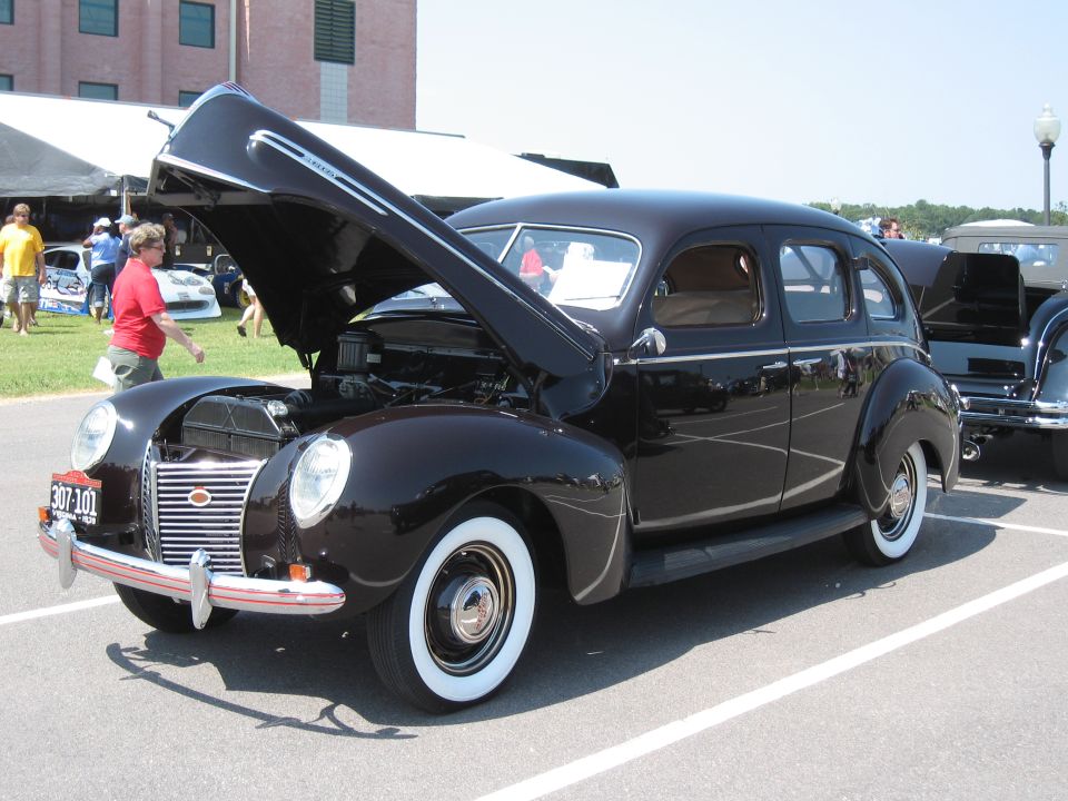 Dark sedan with hood open, showing engine. Whitewall tires, chrome bumper, and grille. License plate reads 307-101
