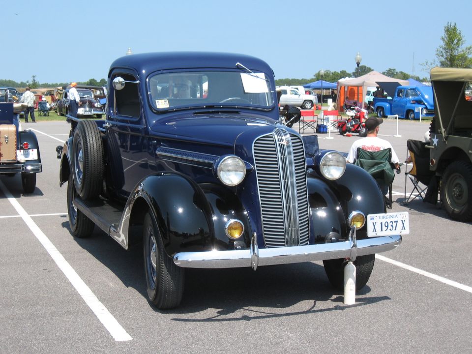 Dark blue 1937 pickup truck with a spare tire on the side, parked at an outdoor event