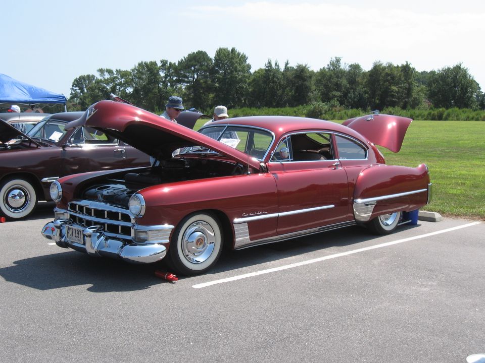 Red 1950s Cadillac coupe with hood and trunk open, parked next to another car