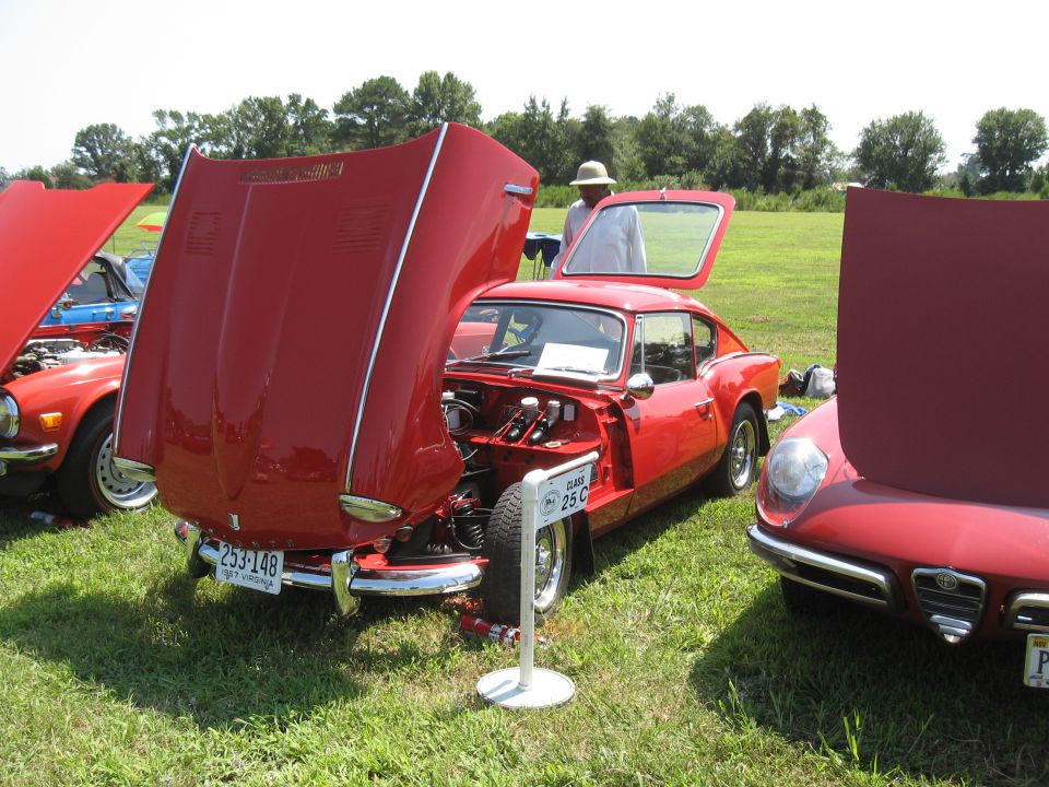 Three red sports cars parked on grass, two with hoods open. One car has a sign that says CLASS 25 C
