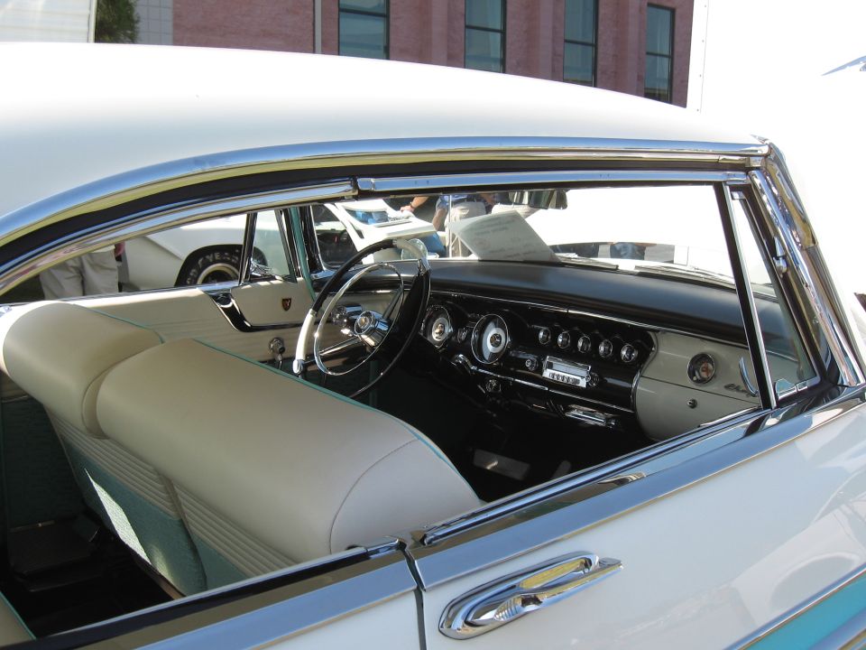 View of a car's interior, showing the dashboard, steering wheel, and seats. Another car is visible through the window