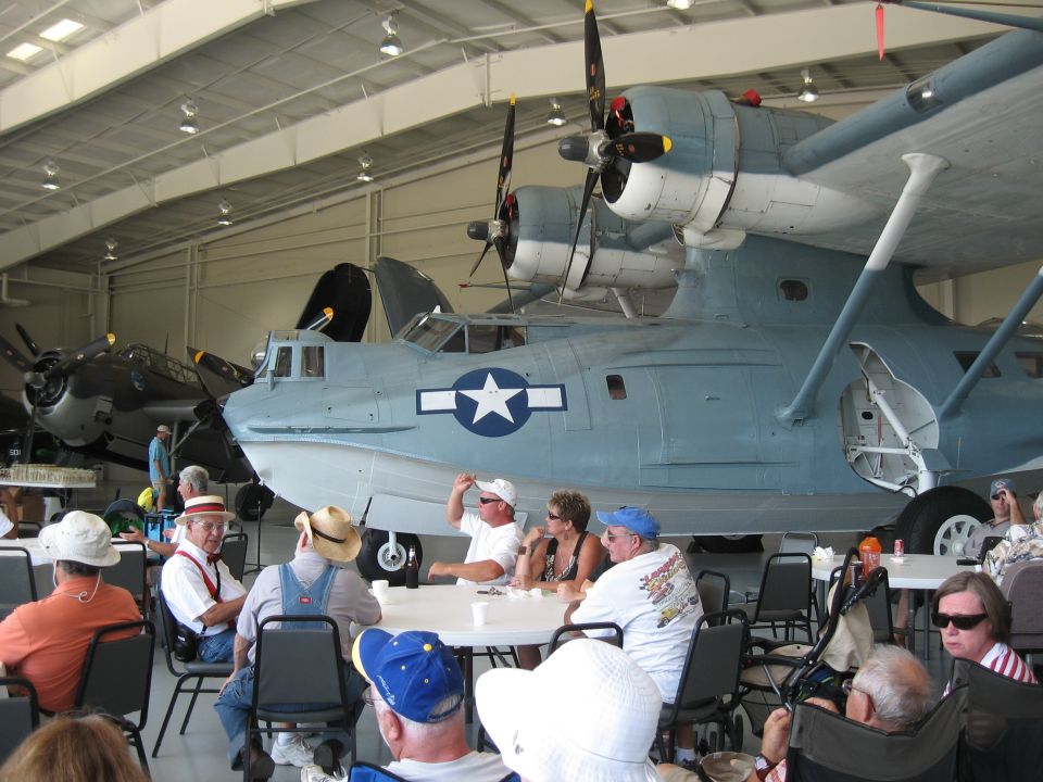 Large seaplane in hangar with people gathered around tables
