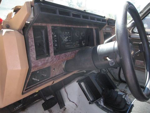 1986 Ford Bronco - The interior dashboard of a vehicle shows analog gauges and a wood-grain trim panel.