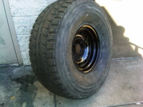 1986 Ford Bronco - A BFGoodrich tire mounted on a black steel rim rests on a concrete surface.