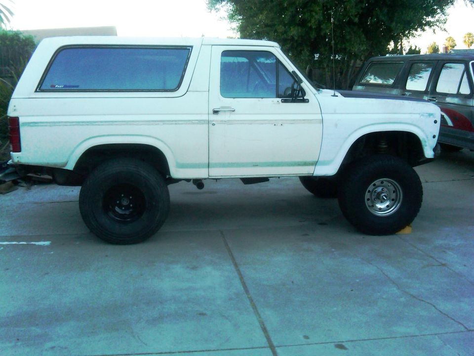 1986 Ford Bronco lifted with large off-road tires, parked next to another vehicle