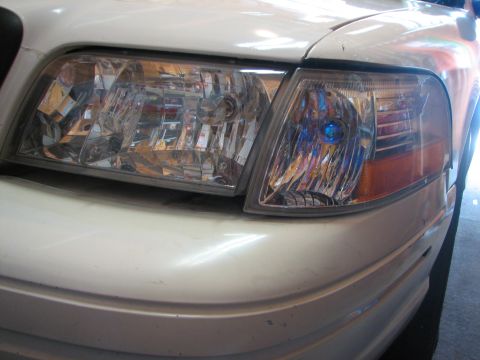 2003 Ford Crown Victoria - Close-up of the front of a white 2003 Ford Crown Victoria, focusing on the headlights and bumper.