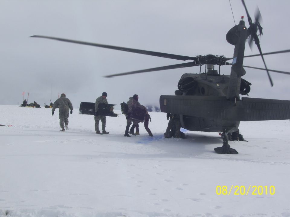 Rear view of a dark helicopter on a snowy plain with personnel unloading cargo