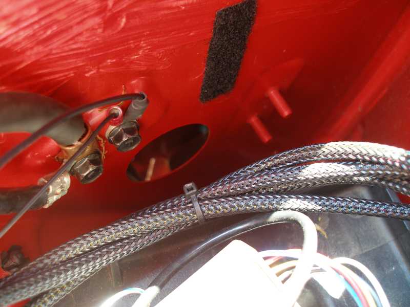 Red painted metal with battery terminals, wires, and braided cable loom. A black velcro patch is visible