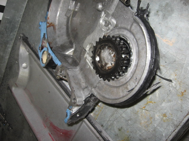 Aluminum timing cover on bench with toothed crank gear and torn seal remnants