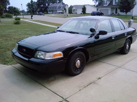 2003 Ford Crown Victoria - Black 2003 Ford Crown Victoria police car parked on a driveway with houses in the background.