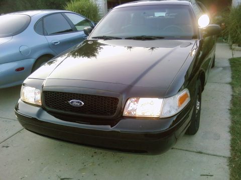 2003 Ford Crown Victoria - A black Ford Crown Victoria is parked on a driveway, with another vehicle to its left.