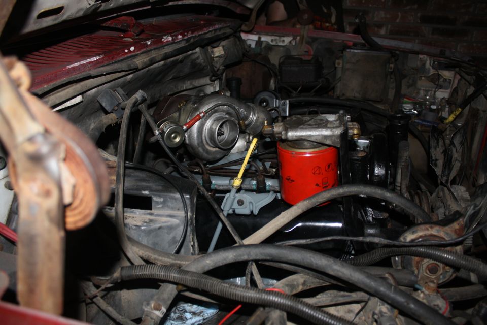 Engine bay with turbocharger, red fuel filter, and various hoses. Some red paint visible on the firewall