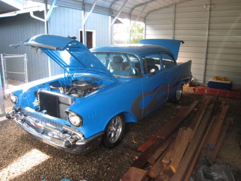 1957 Chevrolet Bel Air - 1957 Chevrolet sedan with flame decals, hood and trunk open, parked in a garage.