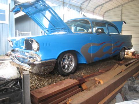 1957 Chevrolet Bel Air - A blue 1957 Chevrolet Bel Air with flame decals sits in a garage with its hood and trunk open.