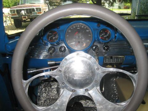 1957 Chevrolet Bel Air - The interior of a classic Chevrolet shows a custom steering wheel and dashboard gauges, with a Ford pickup truck in the background.