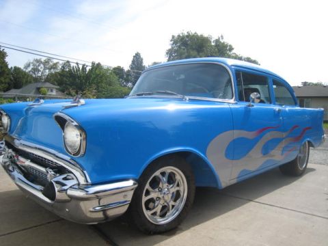 1957 Chevrolet Bel Air - A blue 1957 Chevrolet Bel Air sedan with custom flame graphics is parked outdoors.