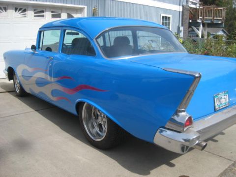1957 Chevrolet Bel Air - A blue 1957 Chevrolet sedan with flame decals is parked in front of a garage.