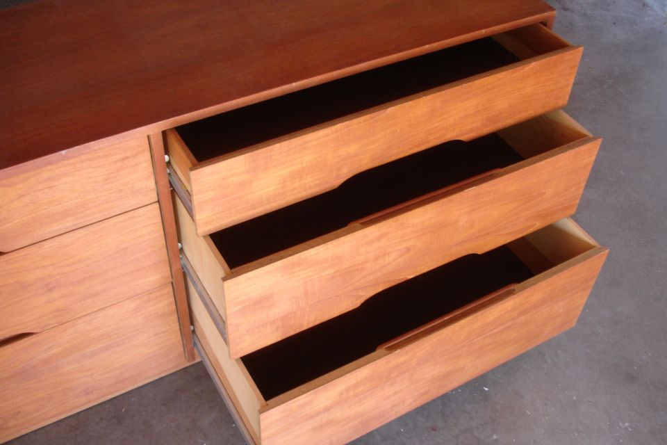 Wooden dresser with three open drawers showing dark interiors