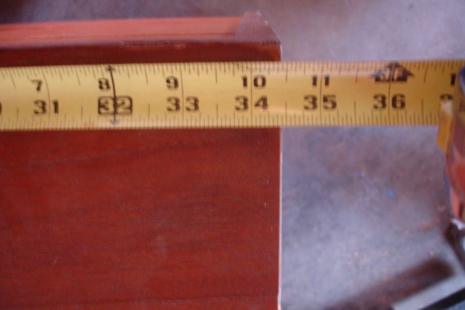 Yellow measuring tape showing inches 31 through 36 laid across a dark red wooden surface