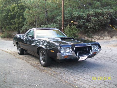 1972 Ford Ranchero - A black 1972 Ford Ranchero is shown from a three-quarter front view on a paved road with trees in the background.