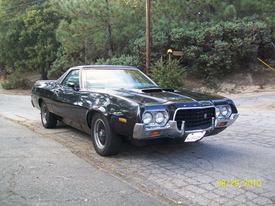 Black Ford Ranchero car-pickup, front three-quarter view, parked on road by trees