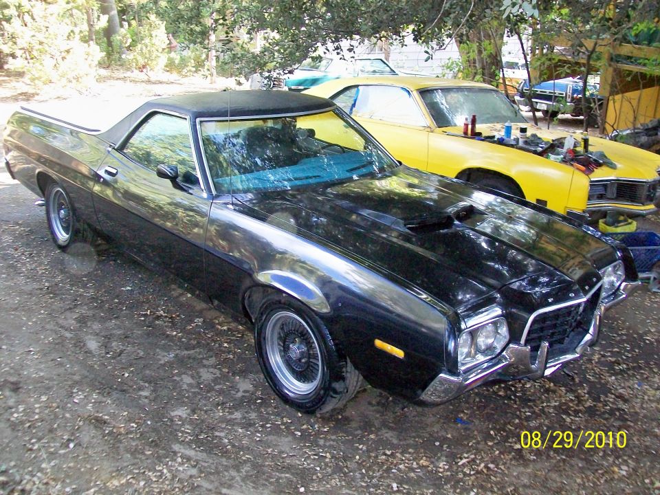 Black Ford Ranchero pickup truck parked outside, yellow car in background