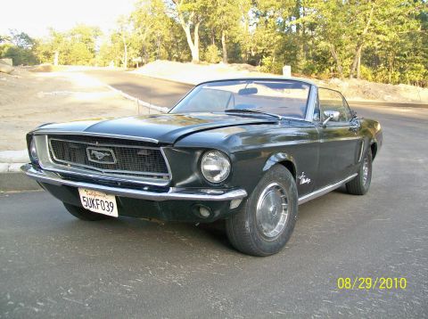 Black convertible Mustang parked on a road, front quarter view. License plate 5UKF039