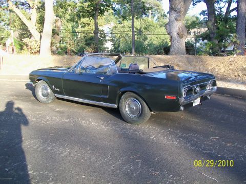 1968 Ford Mustang convertible, dark green, parked on asphalt. Shadow of photographer visible on left