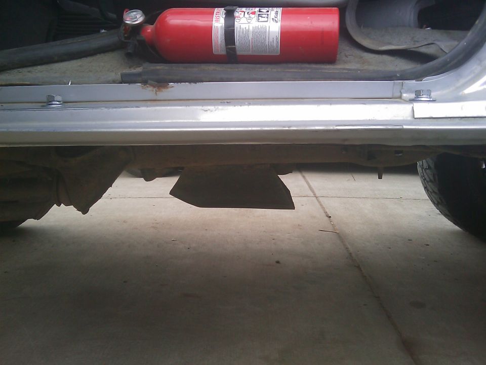 Ground-level view of silver rocker panel and rusty underbody with fire extinguisher on door sill